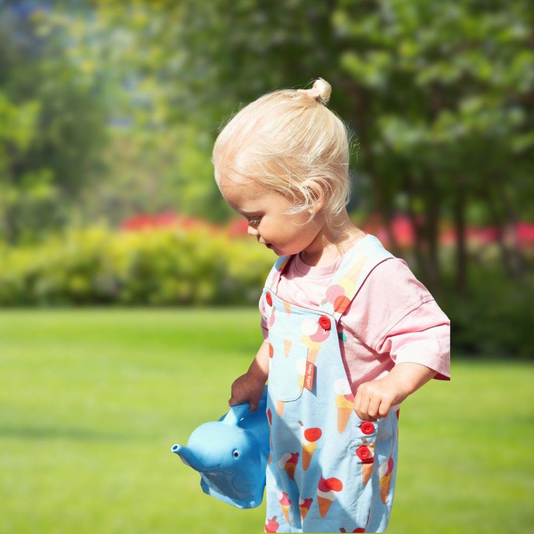 Child holding a blue toy in a park with green grass and trees in the background