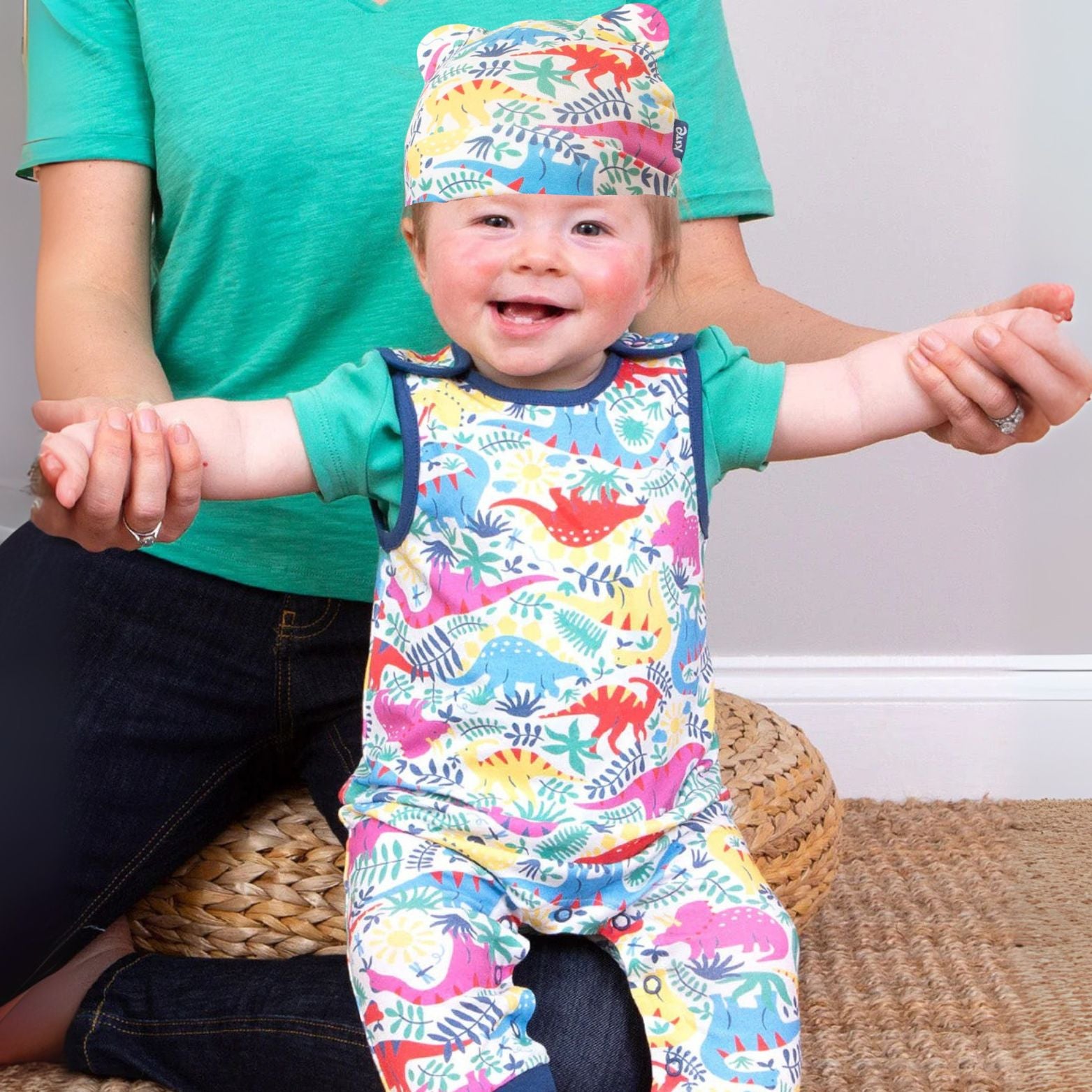 Baby in colorful dinosaur outfit and hat held by an adult