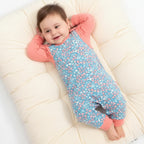 Baby lying on a white surface wearing a blue and pink outfit with a pattern.