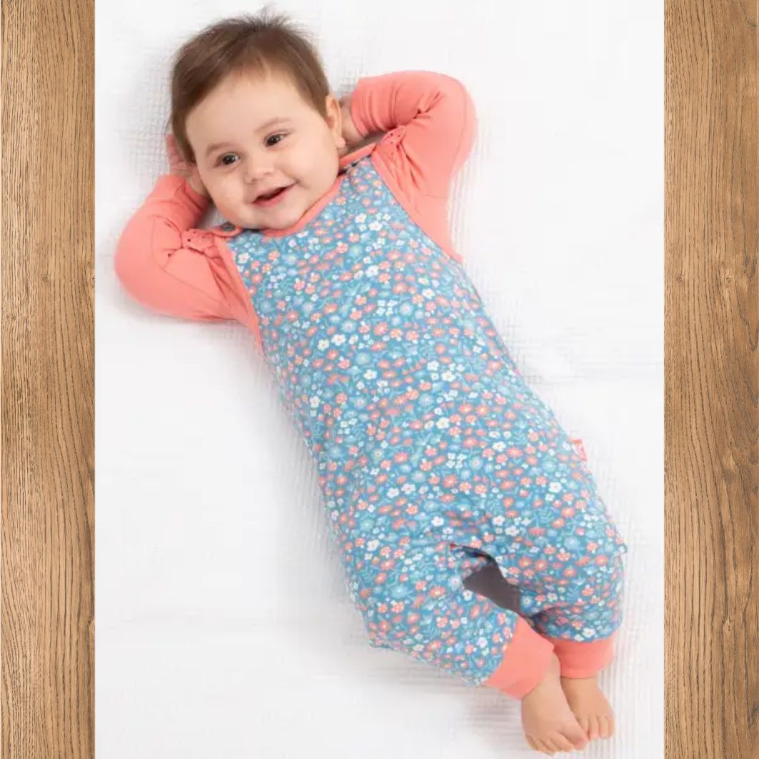 Baby lying on a white surface wearing a blue and pink outfit with a pattern.