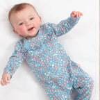 Baby wearing a blue floral onesie lying on a white surface with wooden sides.