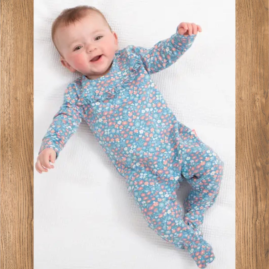 Baby wearing a blue floral onesie lying on a white surface with wooden sides.