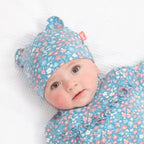 Baby in blue floral outfit and hat on a wooden floor