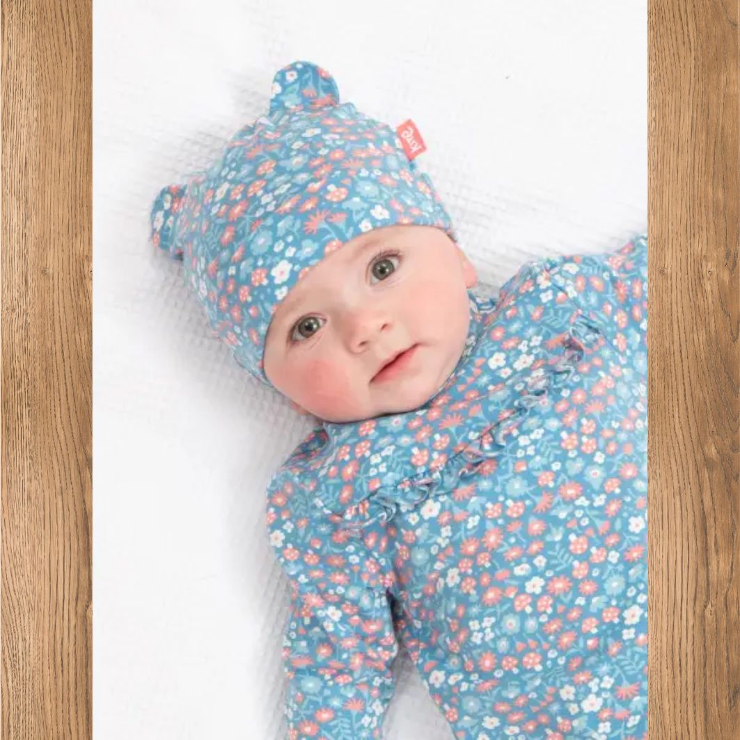 Baby in blue floral outfit and hat on a wooden floor