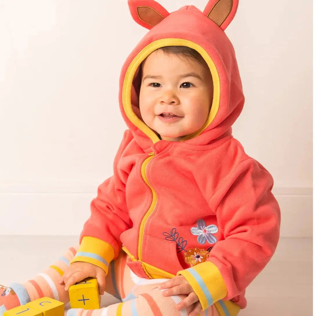 Child wearing a pink hooded outfit with bunny ears on a light background