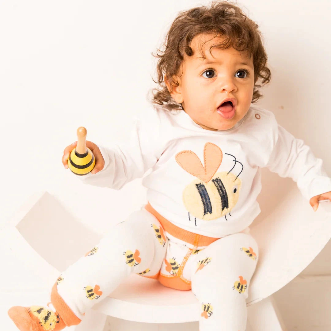 Child wearing a white outfit with bee designs on a white background