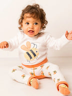 Baby wearing a white outfit with bee designs on a white background