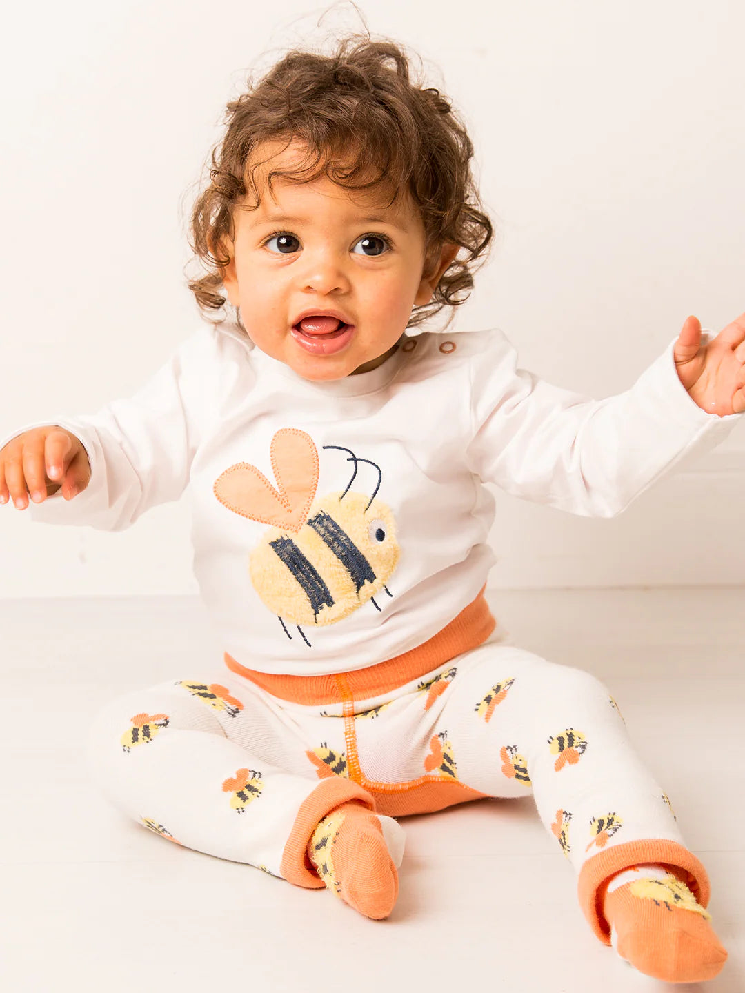 Baby wearing a white outfit with bee designs on a white background