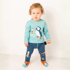 Child wearing a light blue long-sleeve shirt with penguin design and blue pants with nautical patterns on a white background