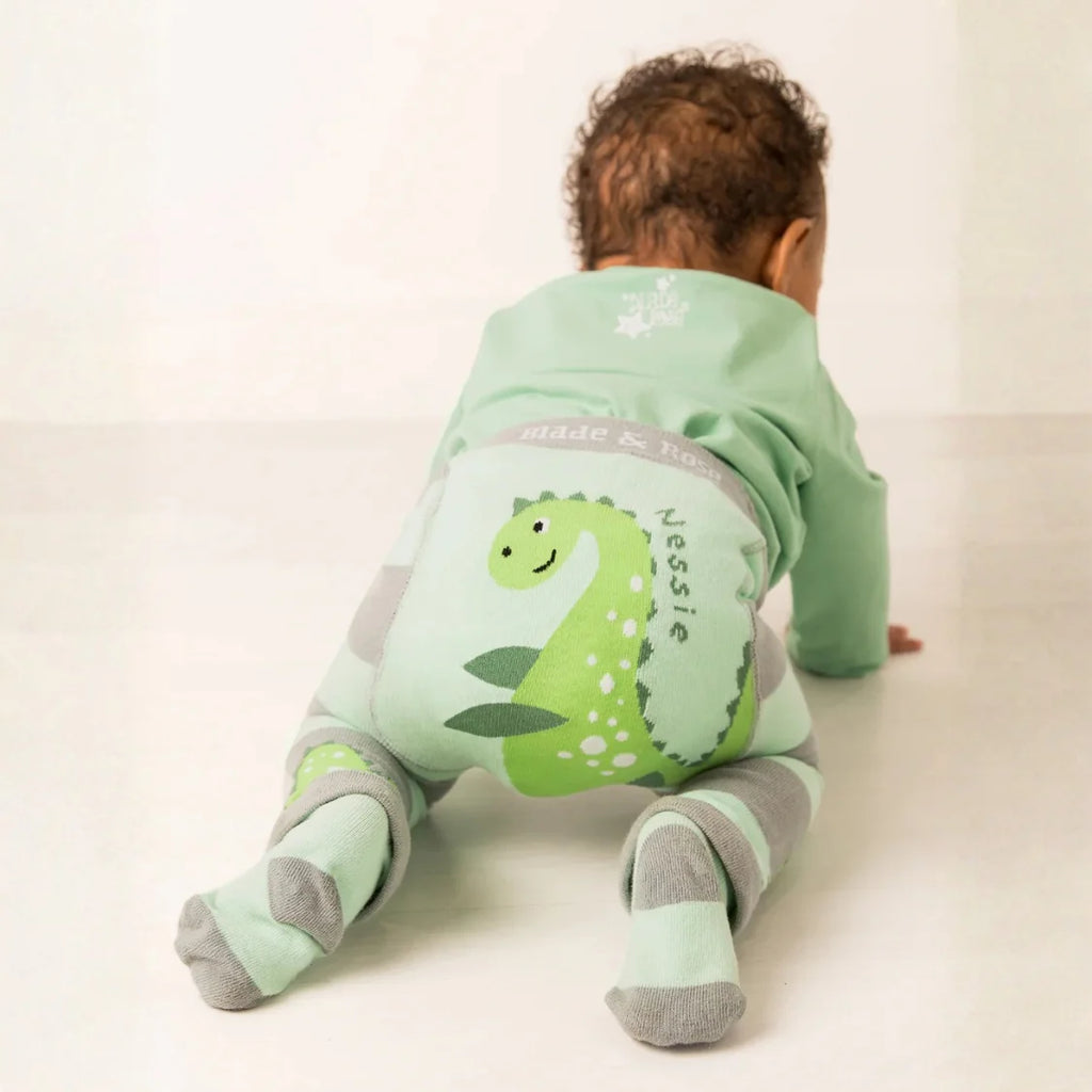 Baby wearing a green dinosaur-themed onesie on a white background