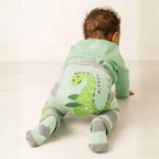 Baby wearing a green dinosaur-themed onesie on a white background