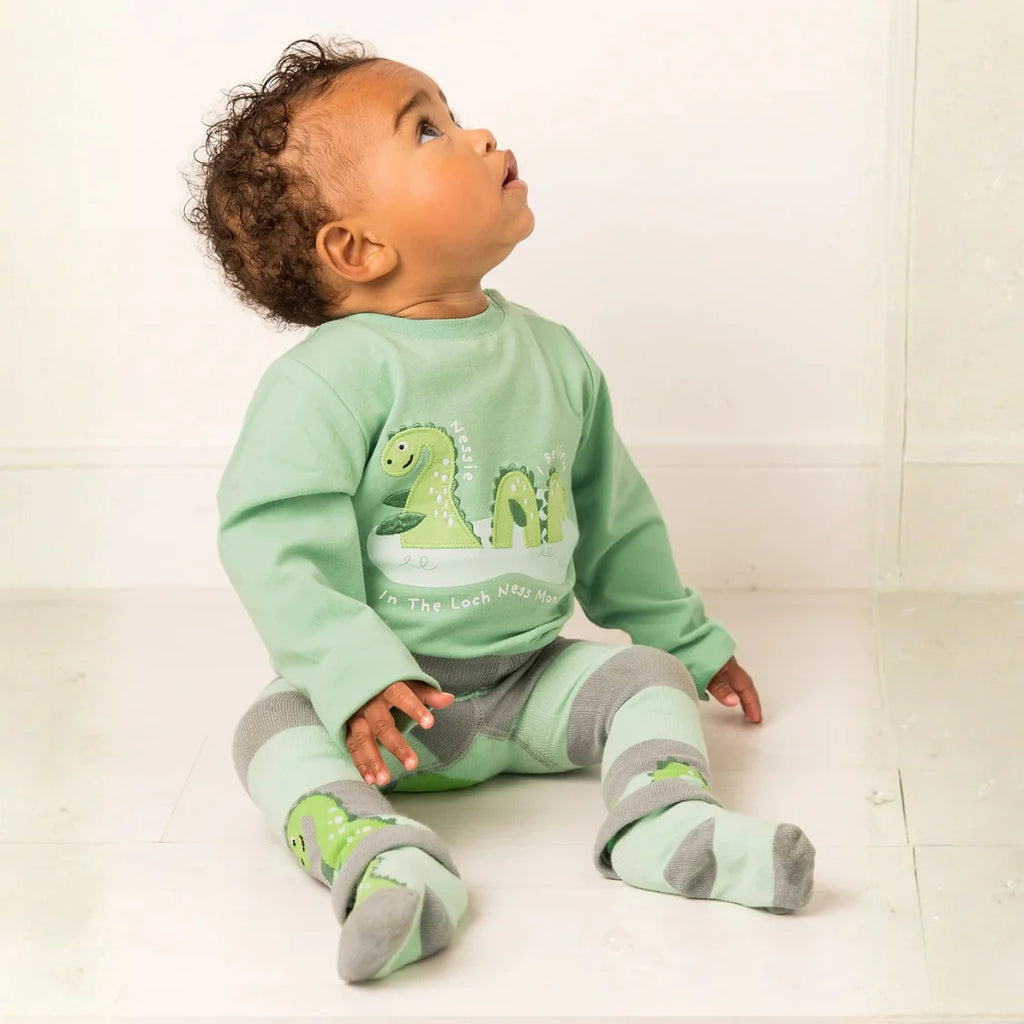 Baby wearing a green dinosaur-themed outfit sitting on a white floor.
