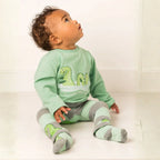 Baby wearing a green dinosaur-themed outfit sitting on a white floor.
