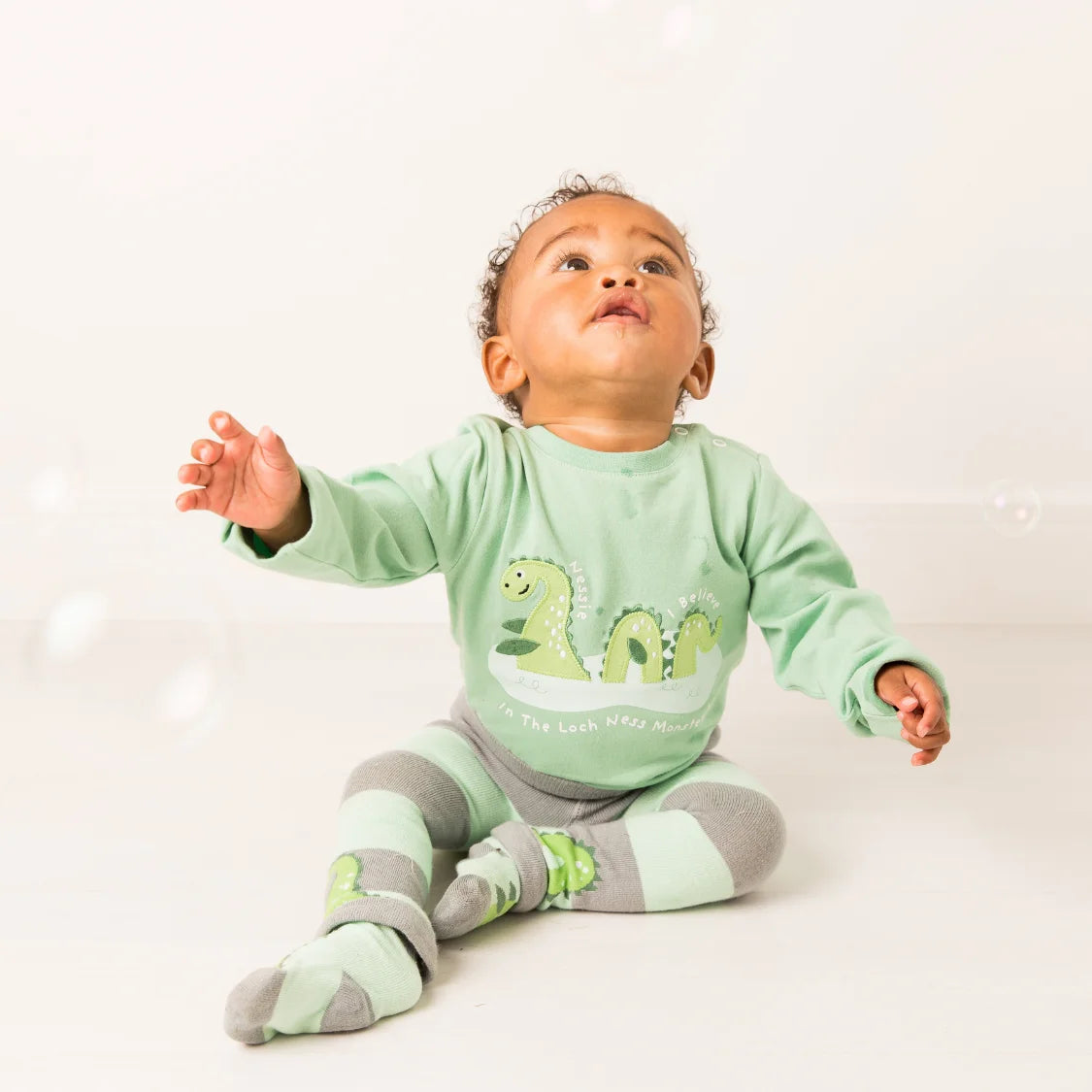 Baby wearing a green dinosaur-themed outfit on a white background
