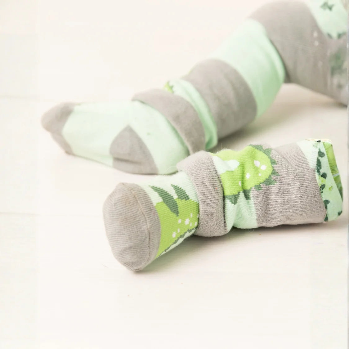 Pair of green and gray socks with dinosaur design on a light background