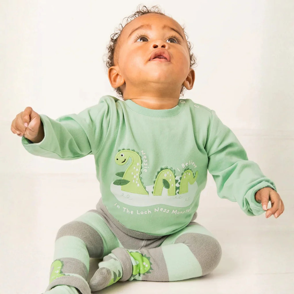 Baby wearing a green outfit with dinosaur design on a white background