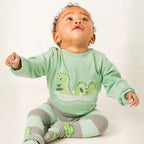 Baby wearing a green outfit with dinosaur design on a white background