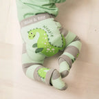Green and gray baby romper with dinosaur design and 'Made & Rose' branding on a beige background.