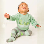Baby wearing a green outfit with dinosaur graphics on a white background