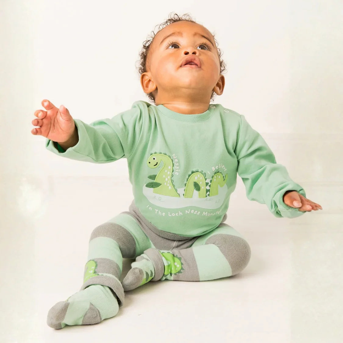 Baby wearing a green outfit with dinosaur graphics on a white background
