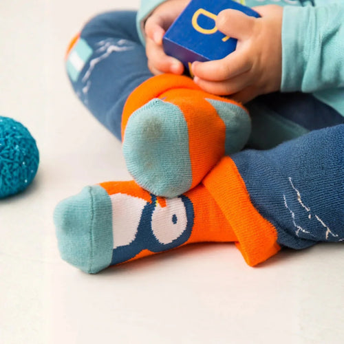 Child wearing colorful socks with cartoon design, sitting on a white surface.