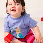 Child wearing a blue shirt with a cartoon character, holding red blocks.