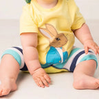 Baby wearing a yellow shirt with a rabbit design and striped pants on a white background