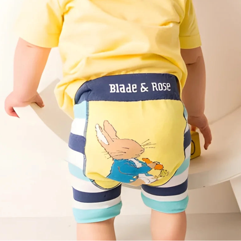 Child wearing a yellow shirt and striped shorts with a visible brand logo, standing on a white surface.