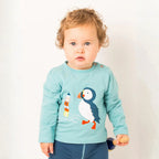 Child wearing a light blue shirt with a puffin design on a plain background
