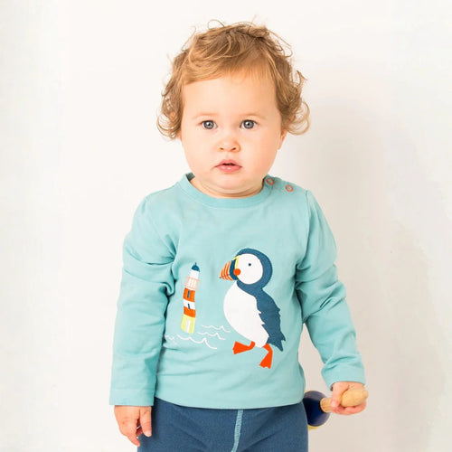 Child wearing a light blue shirt with a puffin design on a plain background