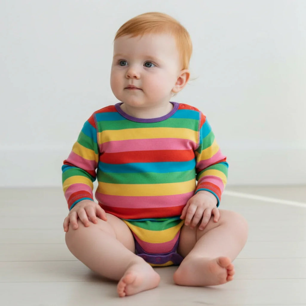 Baby wearing a colorful striped onesie sitting on a white floor.