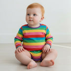 Baby wearing a colorful striped onesie sitting on a white floor.