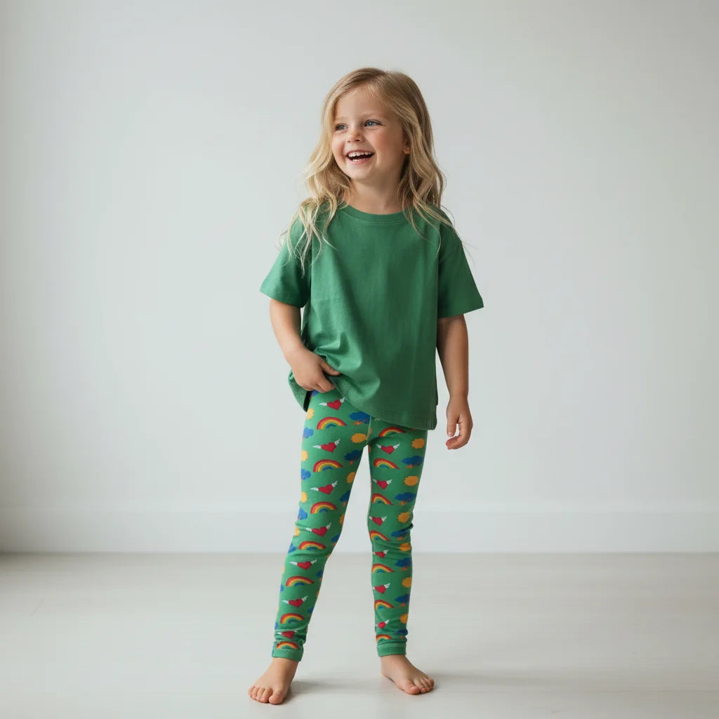 Child wearing green pajama set with rainbow pattern on a plain background