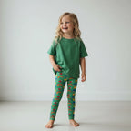 Child wearing green pajama set with rainbow pattern on a plain background