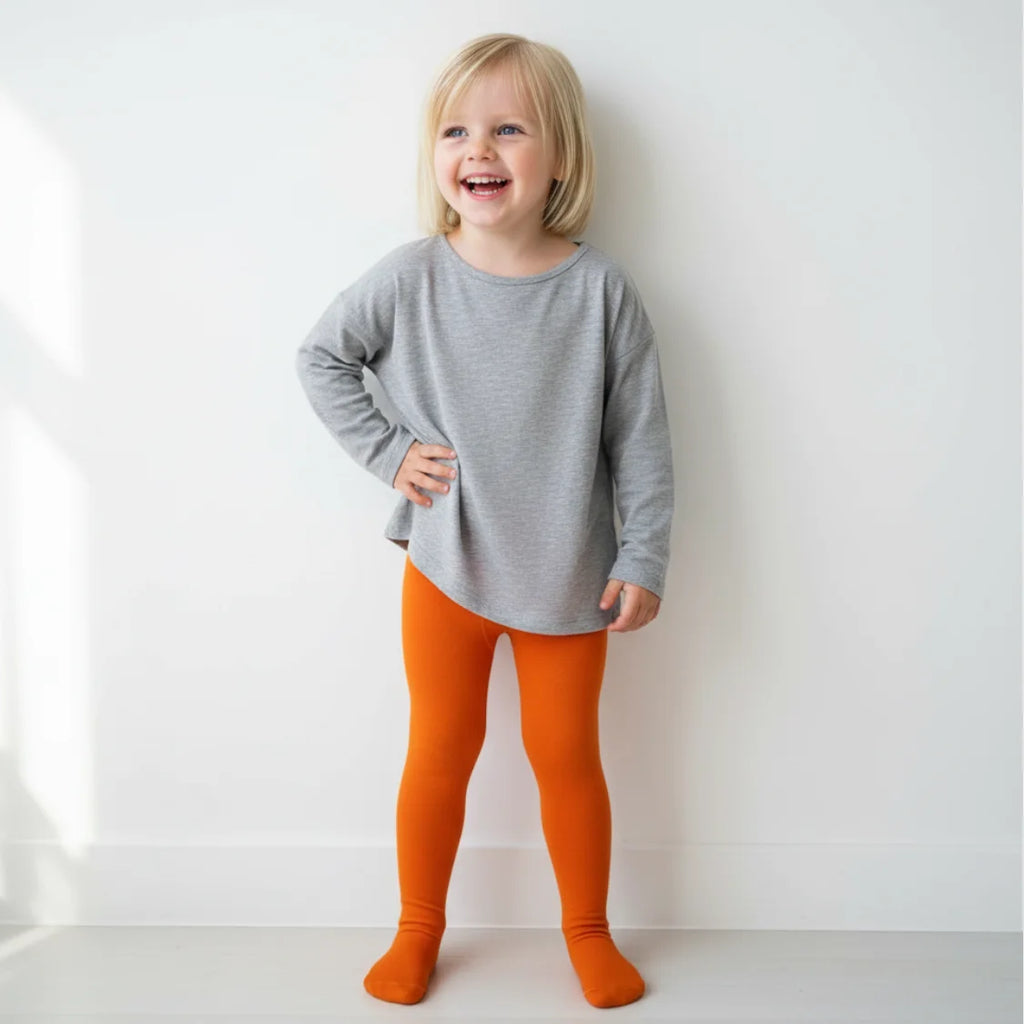 Child wearing a gray long-sleeve shirt and orange leggings against a white background