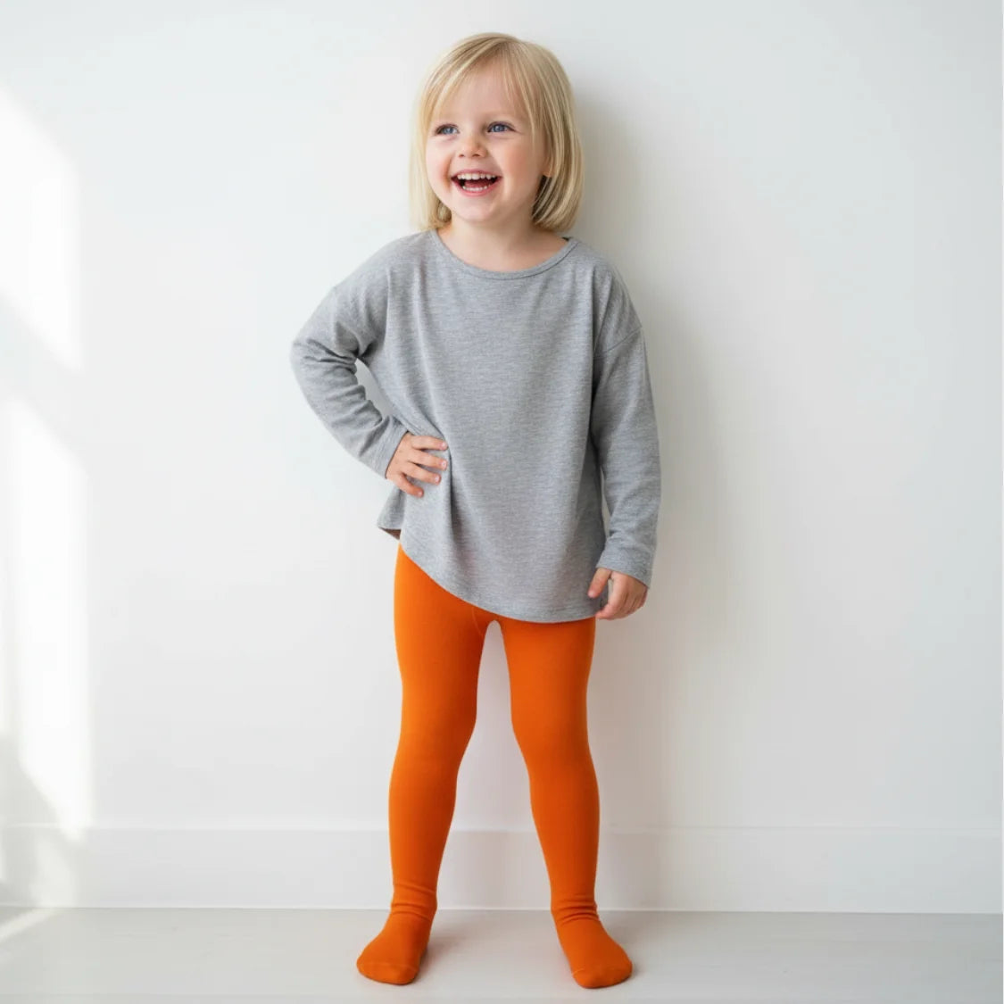 Child wearing a gray long-sleeve shirt and orange leggings against a white background
