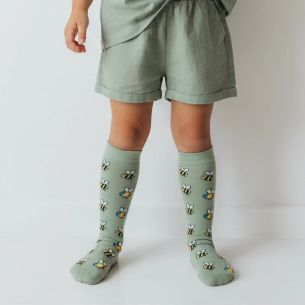 Child wearing green knee-high socks with bee pattern on a plain background