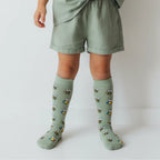 Child wearing green knee-high socks with bee pattern on a plain background