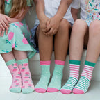 Three children wearing colorful socks with patterns on a white floor.