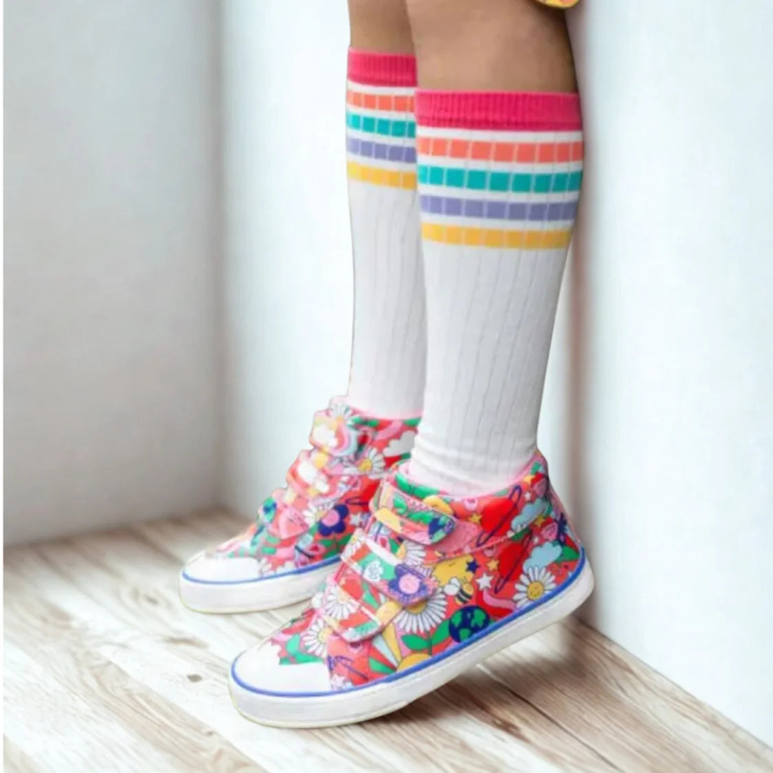 Colorful floral sneakers with white socks and rainbow striped leg warmers on a light wooden floor.