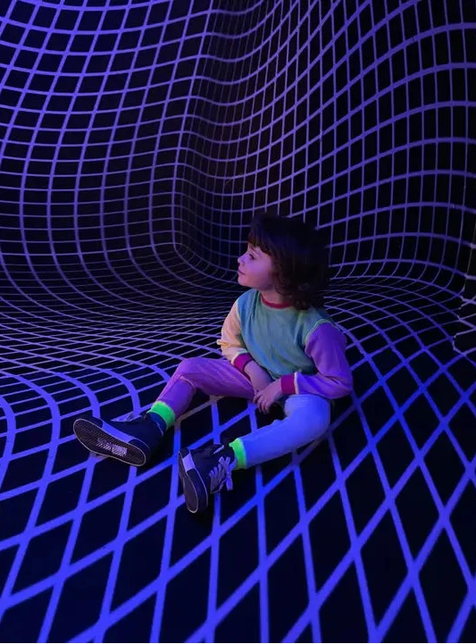 Person sitting on a grid-like floor with a wavy pattern, wearing colorful clothing.