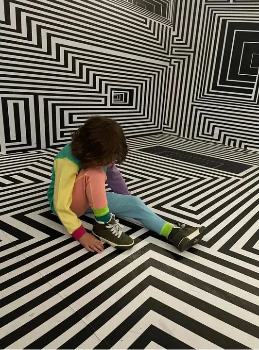 Person sitting on a black and white striped floor with matching walls.