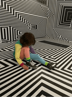 Person sitting on a black and white striped floor with matching walls.