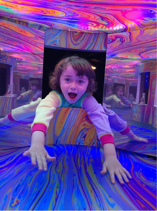 Child in a colorful, reflective room with swirling patterns.