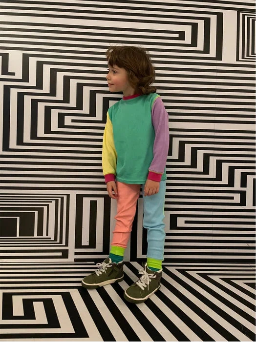 Child wearing a colorful outfit standing in front of a black and white geometric patterned wall.