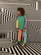 Child wearing a colorful outfit standing in front of a black and white geometric patterned wall.
