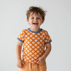 Child wearing an orange patterned shirt with blue trim on a plain background