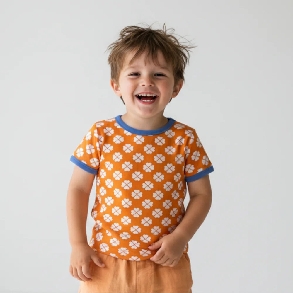 Child wearing an orange patterned shirt with blue trim on a plain background