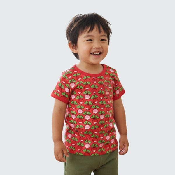 Child wearing a red t-shirt with a pattern of green leaves and pink radish on a white background
