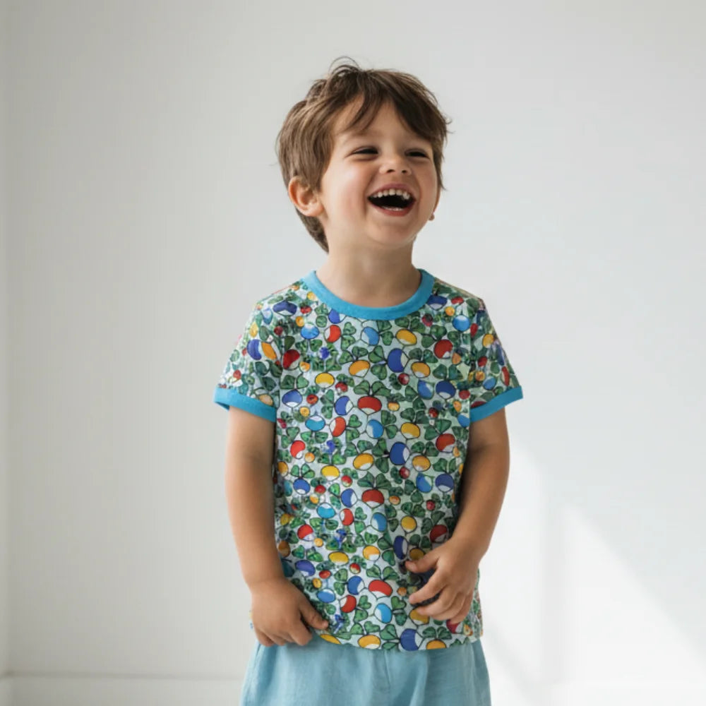 Child wearing a colorful patterned shirt and light blue pants against a plain background